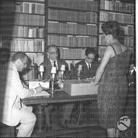 Luigi Barzini seduto ad una scrivania durante le votazioni preliminari per lo Strega 1963 in casa Bellonci; di lato (con un vestito bianco) Giuseppe Gironda - piano medio